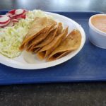 Tacos topped with radishes, cabbage, and sauce, served on a blue tray for a colorful Mexican dish